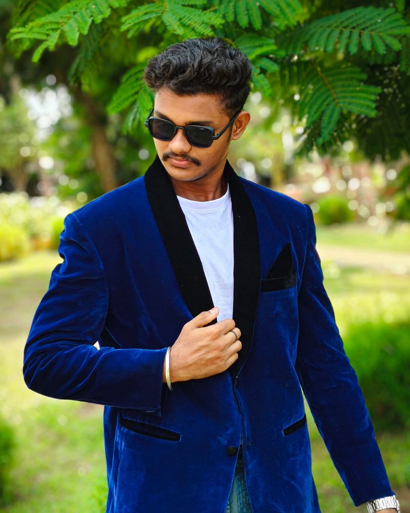 Sushant Tare outdoors under a tree, wearing a navy velvet blazer and sunglasses.
